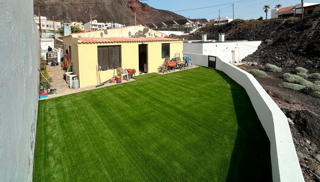Cada vez más personas eligen instalar césped artificial en sus jardines, terrazas y espacios de uso compartido. No es casualidad. Su aspecto cuidado, su resistencia al clima y lo poco que exige han convertido esta solución en una de las más prácticas y cómodas para quienes valoran el bienestar sin complicaciones. Aun así, es normal que surjan preguntas antes de dar el paso. En este artículo te ayudamos a resolverlas y a dejar atrás ideas anticuadas. Porque si hay algo que el césped artificial ha demostrado, es que puede transformar cualquier rincón en un lugar listo para disfrutar. ¿Qué es realmente el césped artificial hoy? Olvídate de aquella imagen antigua del césped artificial rígido, brillante y poco convincente. Hoy en día, los materiales han evolucionado tanto que cuesta distinguirlos del césped natural. Hay modelos con distintas alturas, densidades, colores y texturas, pensados para adaptarse a cada tipo de espacio y uso. Puedes instalarlo en un jardín familiar, en una terraza, en la entrada de un negocio o en una zona común de una comunidad. Aguanta el uso diario, resiste el sol y no necesita riego ni productos químicos. Además, si eliges bien, te llevas un suelo bonito, duradero y siempre listo, sin esfuerzo. Mitos que ya no tienen sentido Aunque el césped artificial forma parte del día a día en jardines, terrazas y zonas infantiles, todavía hay ideas equivocadas que conviene aclarar. Una de las más comunes es pensar que es tóxico para niños o mascotas. Nada más lejos de la realidad. Los modelos actuales cumplen con normativas europeas y están pensados precisamente para espacios donde se juega, se corre y se disfruta sin preocupaciones. Tampoco es cierto que requiera mucho mantenimiento. Con un simple cepillado ocasional y algo de agua cuando hace falta, el césped artificial se mantiene limpio, suave y con buen aspecto. Sin podas, sin riego y sin productos químicos. ¿Y la durabilidad? Hay modelos diseñados para resistir el uso intensivo, el sol canario y el paso del tiempo sin problema. Además, la idea de que se ve falso ha quedado atrás. Hoy existen versiones tan realistas que cuesta diferenciarlas de un jardín natural, con la ventaja de que el aspecto se mantiene siempre impecable. Lo que sí es: ventajas reales El césped artificial ha ganado terreno por méritos propios. Una de sus mayores ventajas es la tranquilidad que ofrece. No tienes que estar pendiente del riego, ni preocuparte por el calor, las calvas o el barro después de la lluvia. Siempre está ahí, limpio, uniforme y listo para usar. También supone un ahorro considerable. Sin agua, sin productos químicos y sin mantenimiento profesional, los costes a largo plazo se reducen. Además, se adapta bien a todo tipo de espacios: jardines familiares, patios escolares, zonas comunes o terrazas en altura. A nivel estético, el resultado es constante. Verde todo el año, sin esfuerzo. Y si eliges un modelo de calidad, el confort al caminar o sentarse sobre él mejora mucho la experiencia del espacio. En definitiva, es una solución práctica, duradera y pensada para disfrutar más y preocuparse menos. ¿Qué conviene tener en cuenta antes de instalarlo? Aunque el césped artificial tiene muchas ventajas, no todos los modelos sirven para lo mismo. Elegir bien en función del uso previsto es clave. Hay opciones más suaves para zonas infantiles, más resistentes para espacios de paso o más decorativas para terrazas de uso ocasional. En Canarias Verde trabajamos con productos RealTurf, que incorporan tecnologías únicas que otros céspedes convencionales no ofrecen. MaxRecover aporta el efecto memoria que mantiene las fibras siempre erguidas, incluso en zonas de mucho tránsito o con mobiliario encima. Esto significa que tu césped recupera su forma tras cada pisada y conserva su aspecto mullido y uniforme sin esfuerzo. MaxDrain multiplica la capacidad de drenaje, ideal si tienes mascotas o si el césped rodea una piscina. Al evacuar líquidos y suciedad con rapidez, el espacio se mantiene limpio y listo para disfrutar en cualquier momento. Estas innovaciones alargan la vida útil del césped y te dan tranquilidad. Sabes que tu inversión se mantendrá perfecta con un mantenimiento mínimo, algo que convierte a Canarias Verde en la mejor opción para quienes buscan calidad y despreocupación. Así te aseguras de que el resultado sea duradero, cómodo y estéticamente impecable desde el primer día. Una decisión que se nota cada día Instalar césped artificial es mucho más que una mejora estética. Es una forma de ganar tiempo, reducir preocupaciones y crear espacios agradables donde siempre apetece estar. Si eliges bien, lo notarás desde el primer momento: menos mantenimiento, más comodidad y un entorno cuidado durante todo el año. En Canarias Verde llevamos años ayudando a transformar jardines, terrazas y zonas comunes con soluciones pensadas para durar y adaptarse a tu estilo de vida. Porque disfrutar de tu espacio sin complicaciones también es una forma de bienestar.